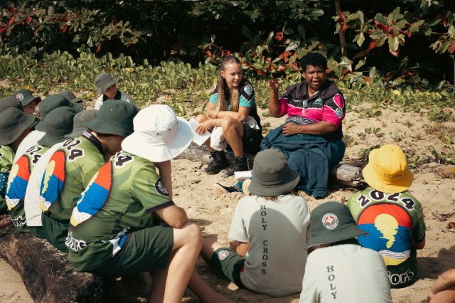 Group of school students on a beach learning from a community science educator 